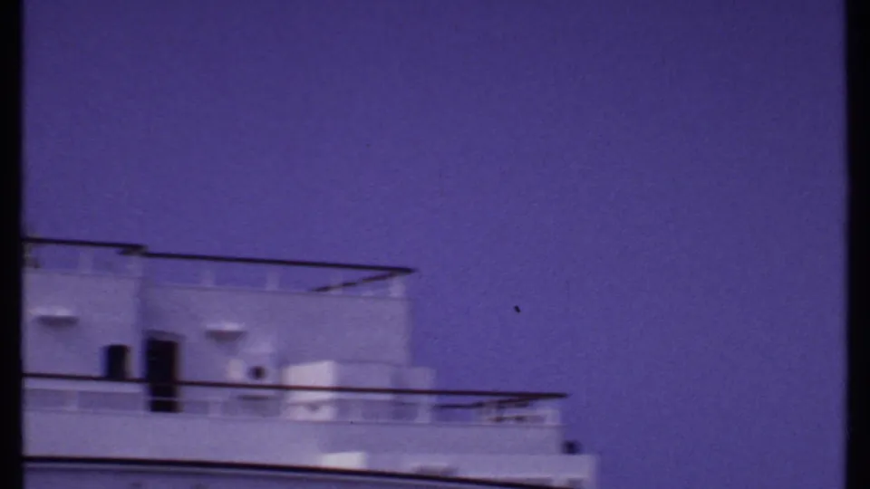 Bahamas 1969 home-movie frame showing white cruise ship decks, railings, and upper structure beneath a saturated blue-purple sky.