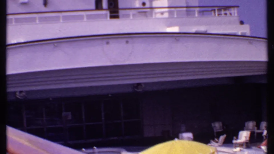 Bahamas 1969 home-movie view of a cruise ship deck with railings, shaded seating, lounge chairs, passengers, and a yellow umbrella.