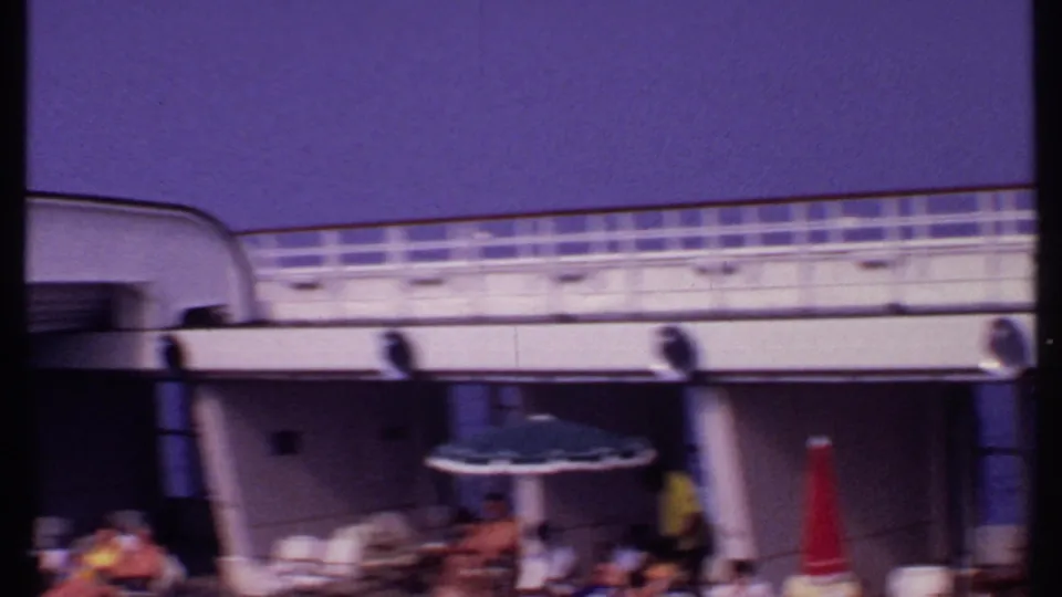 Bahamas 1969 frame showing passengers relaxing on a cruise ship deck below white railings, with umbrellas and lounge chairs visible.