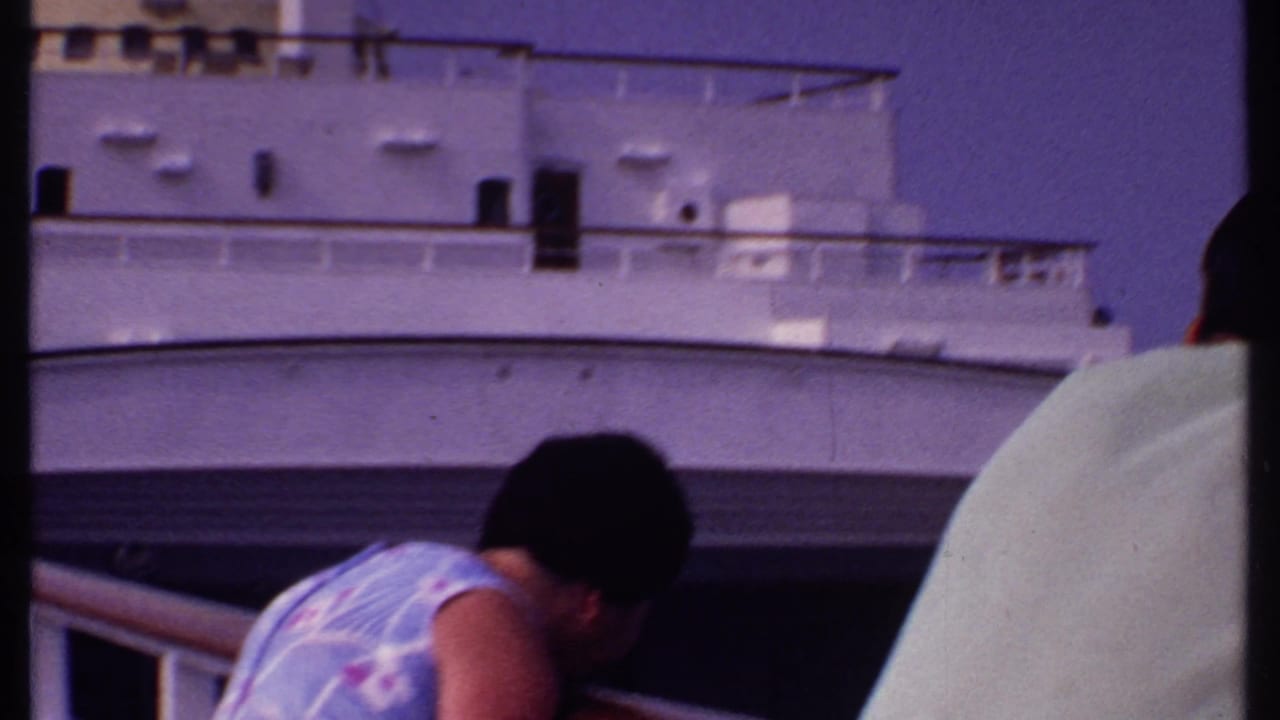 Woman in a floral dress leans near a ship railing beside white decks.