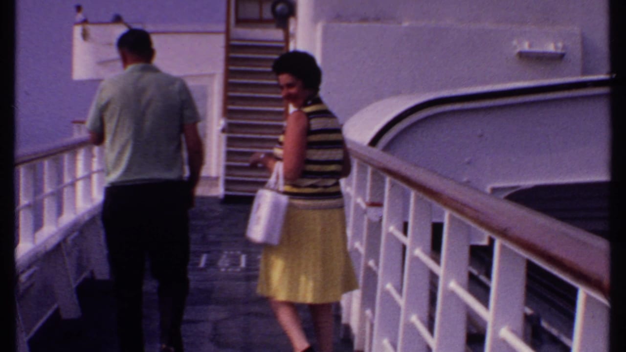 Man and woman stand on a cruise ship deck beside white railings.