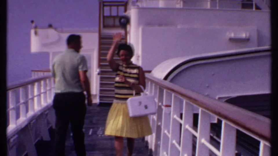 1969 Bahamas cruise deck frame showing the woman waving toward the camera while the man stands nearby by the railings.
