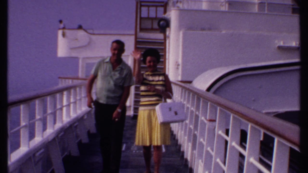 Couple walking along a white-railed ship deck with ocean behind them.