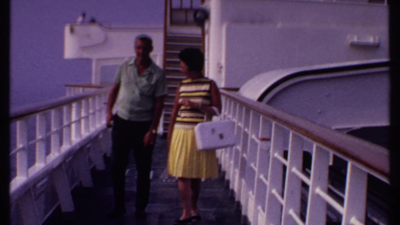 Couple on a ship promenade, walking beside white railings and vessel walls.