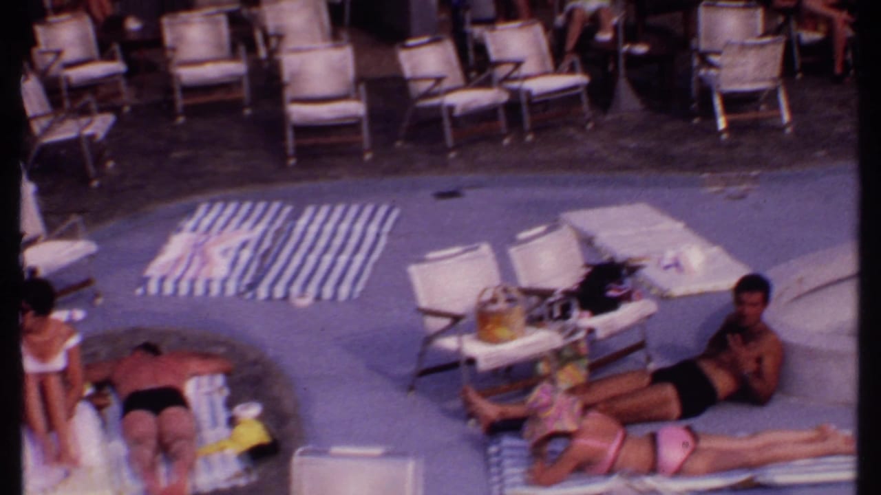Adults at a Bahamian resort pool in 1969 rest on striped towels and lounge chairs in soft 8mm color.