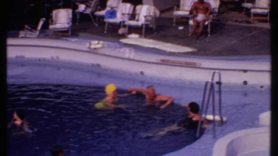 Bahamas resort pool in 1969 with several swimmers in dark water near a metal ladder and lounge chairs beyond the pool edge.