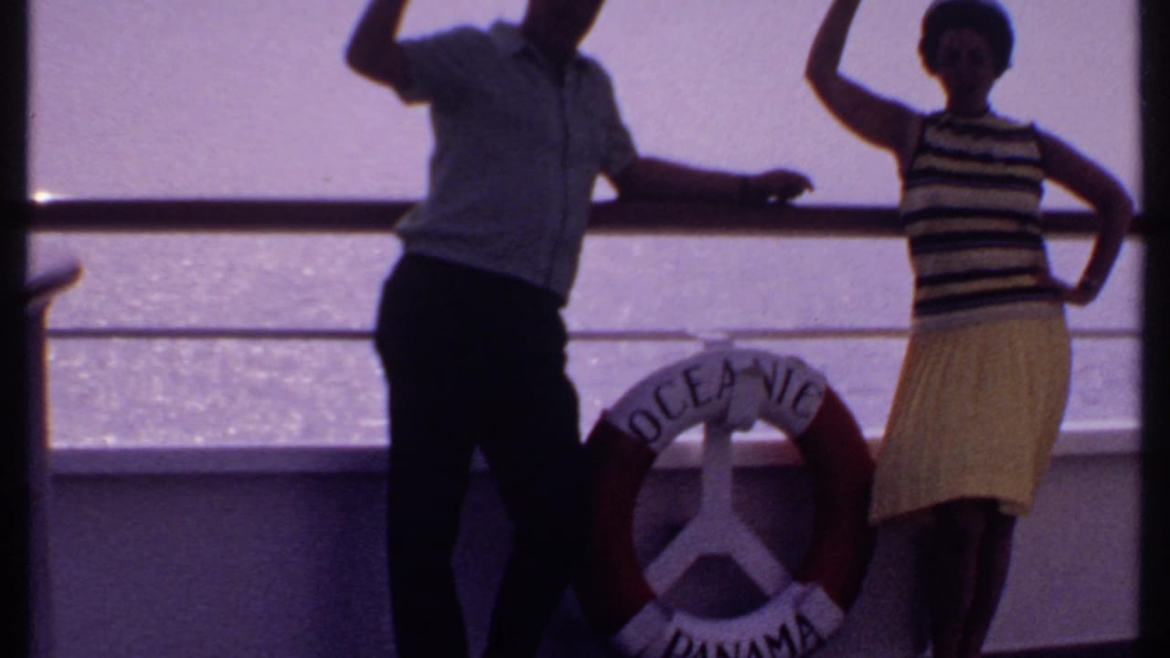 Man and woman pose on a ship deck beside a red and white life ring.