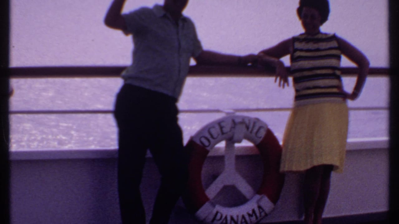 Couple on deck near a life ring, with bright ocean water behind the railing.