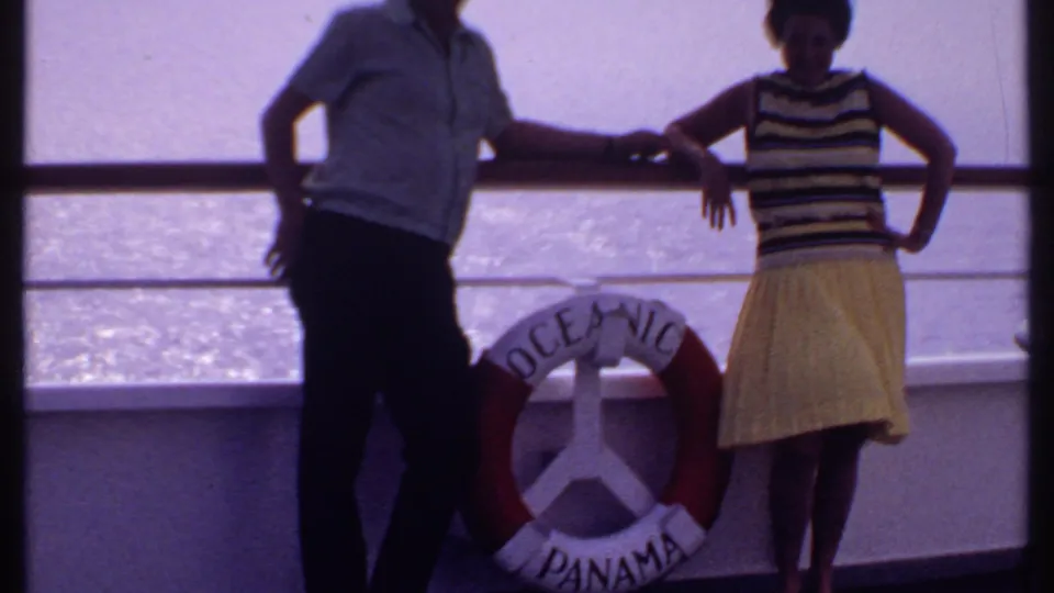 A late-1960s home-movie frame shows the couple closer to the life ring, with the woman's yellow skirt and striped top clearly visible.