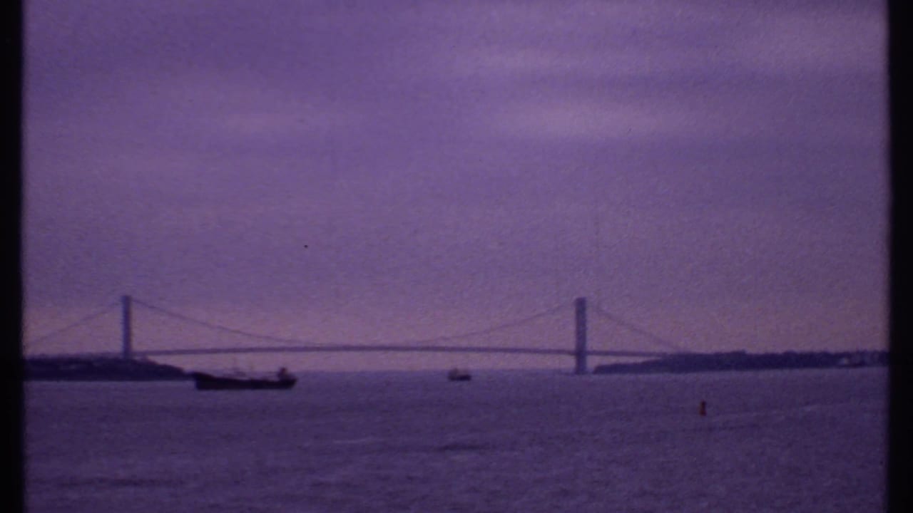 Suspension bridge over open water with boats under a purple evening sky.