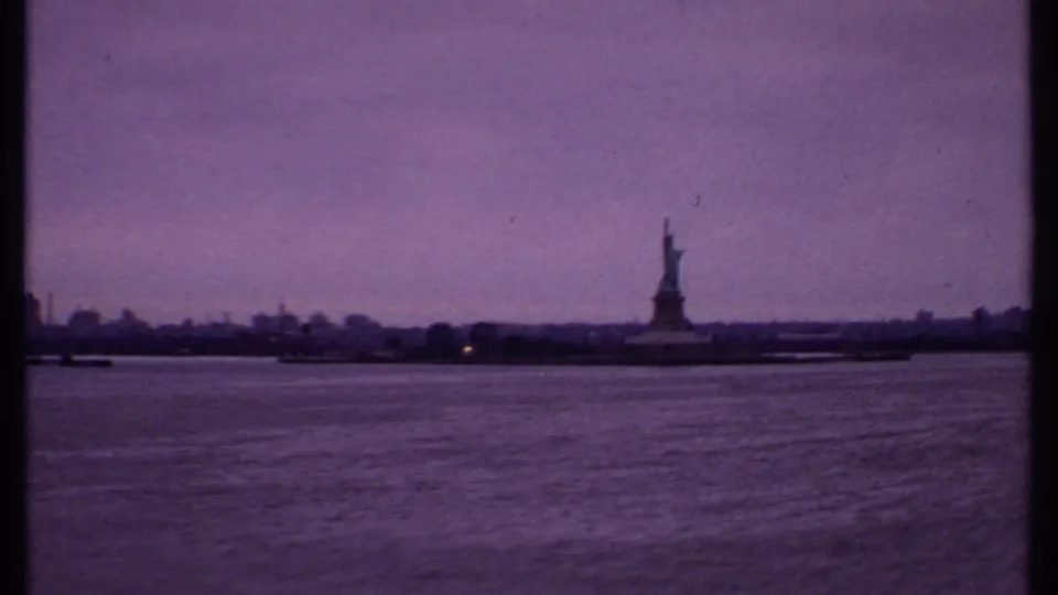 1969 8mm wide view of New York Harbor with the Statue of Liberty, distant skyline, small boats, and visible film gate edges.