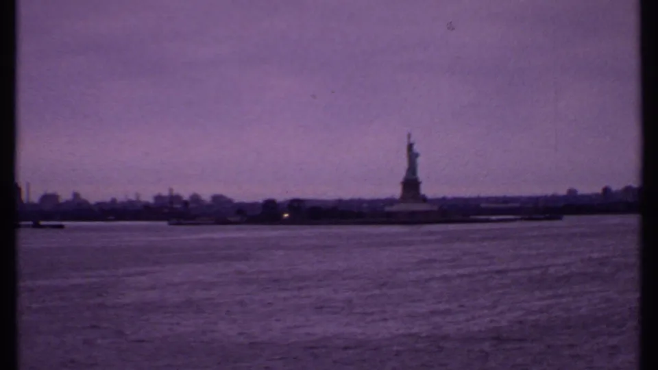 1969 8mm frame showing the Statue of Liberty in the distance across New York Harbor water from a boat.