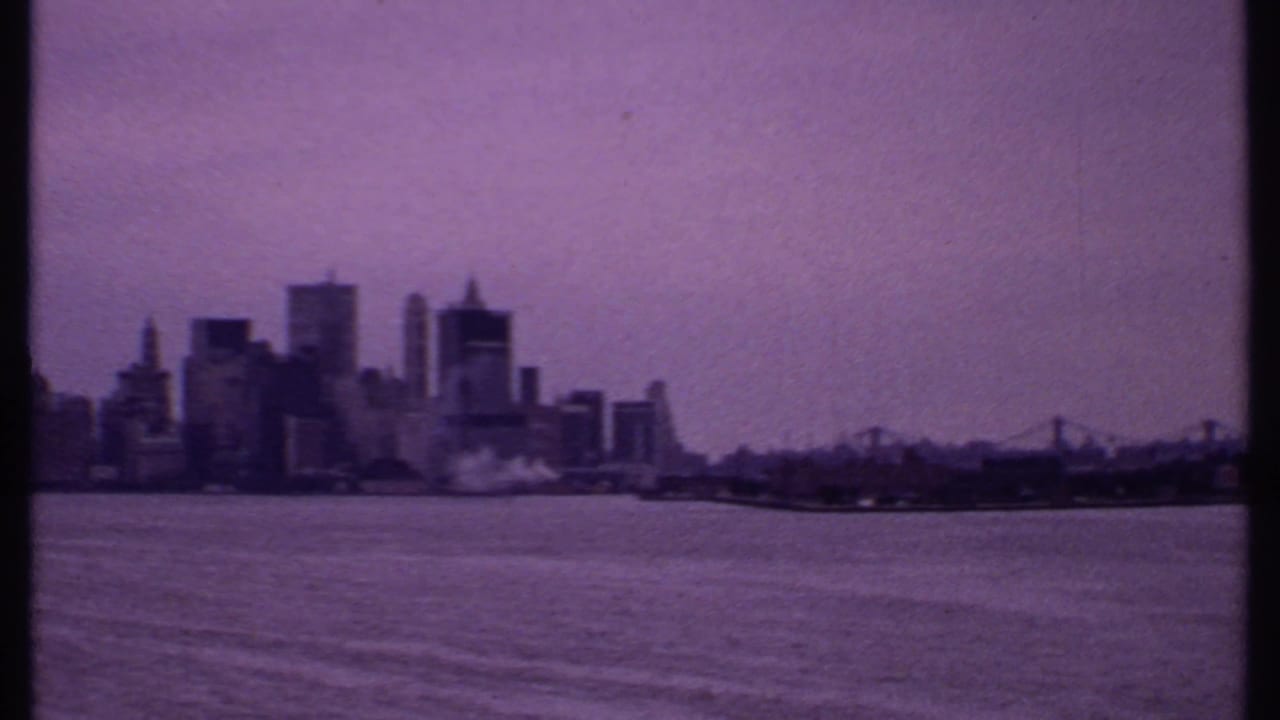 1969 Bahamas 8mm frame showing a distant waterfront skyline and bridge across open water with purple film fading.