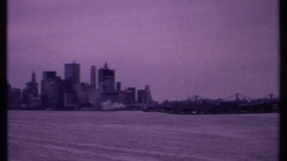 1969 Bahamas 8mm frame showing a distant waterfront skyline and bridge across open water with purple film fading.