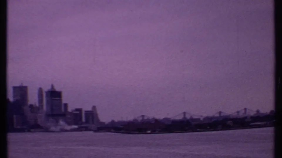 1969 8mm frame showing a distant urban skyline across open water with purple tint and soft film grain.