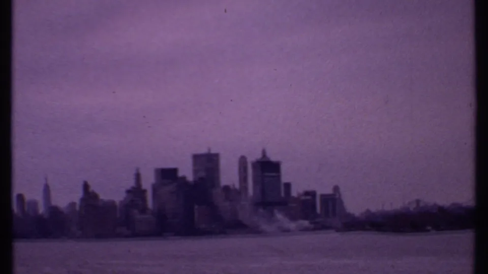 Purple-tinted 8mm view of a distant waterfront city skyline, with high-rise silhouettes across the water.