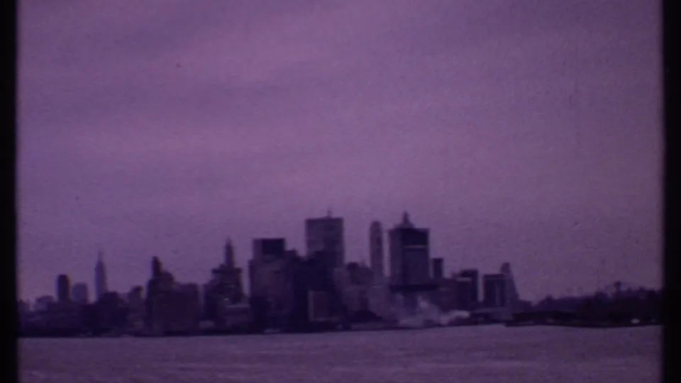 1969 home-movie frame of a distant skyline over water, softened by grain, tint, and exposure variation.