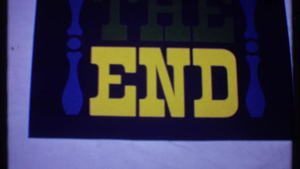 1969 8mm Bahamas reel frame showing a vintage THE END card with yellow letters, green upper text, blue ornaments, and visible film edge.
