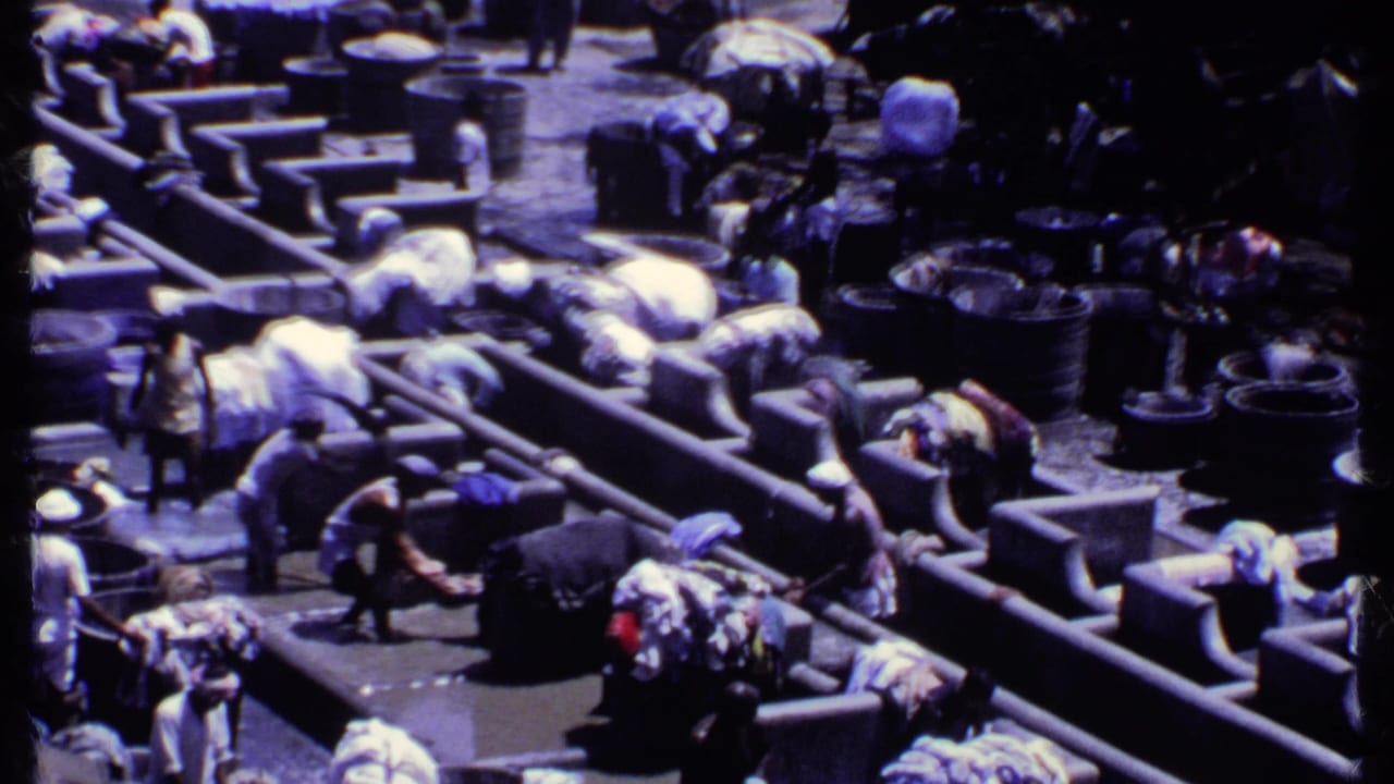 1969 India 8mm frame showing people bending over concrete wash troughs with tubs and laundry bundles around them.