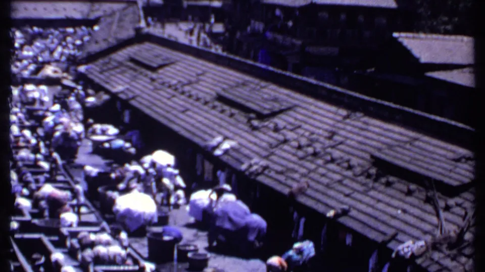 1969 India 8mm frame looking across a corrugated roof toward a busy outdoor laundry facility and surrounding structures.