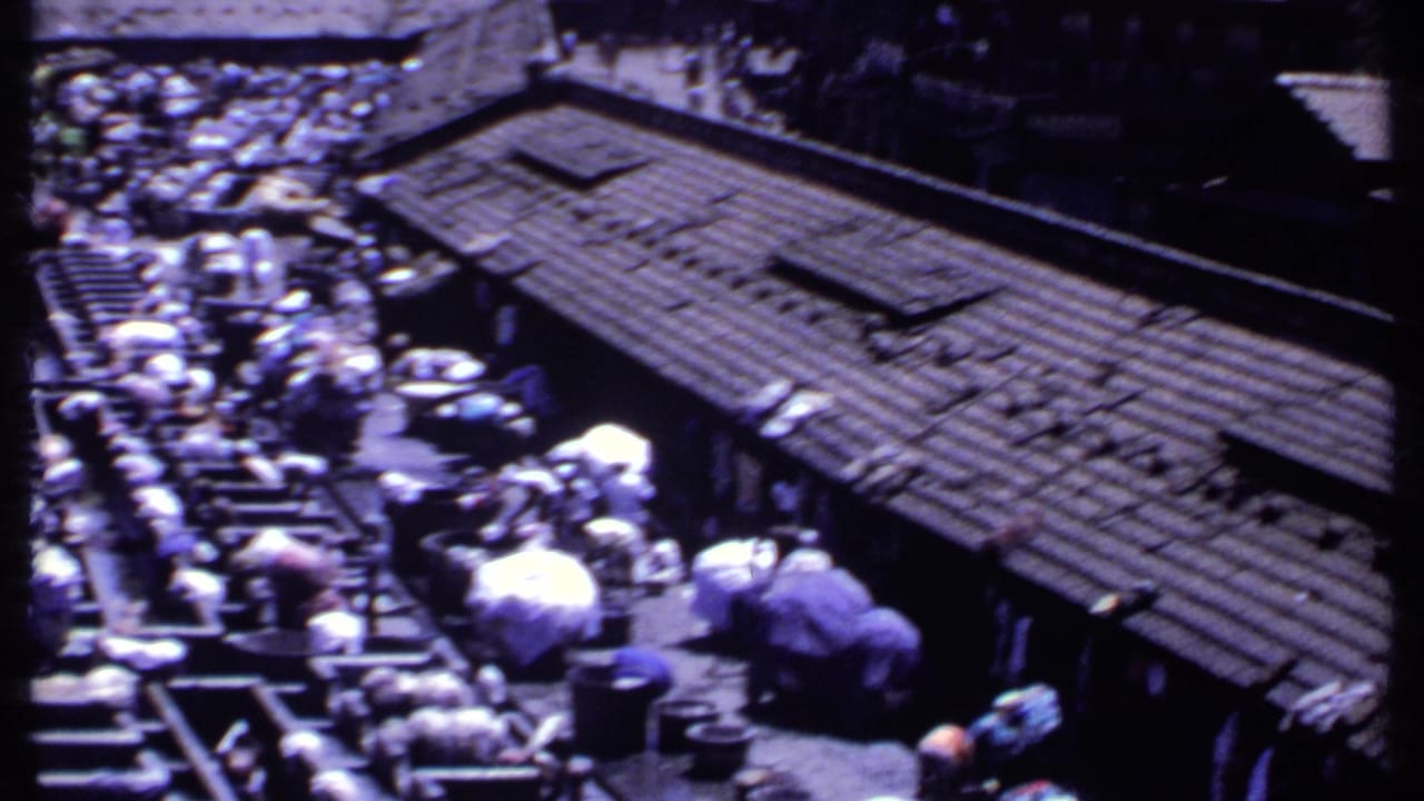 Elevated view of people washing clothes along wooden beams beside a tiled-roof structure.