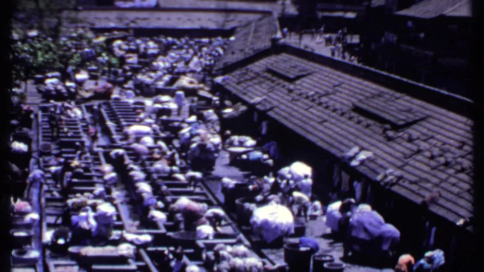 Elevated 1969 India home-movie view of a dense outdoor washing area beside a long tiled-roof building.