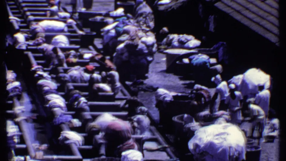 Closer 8mm view of people washing or sorting cloth in a busy outdoor laundry setting in India, based on supplied metadata.