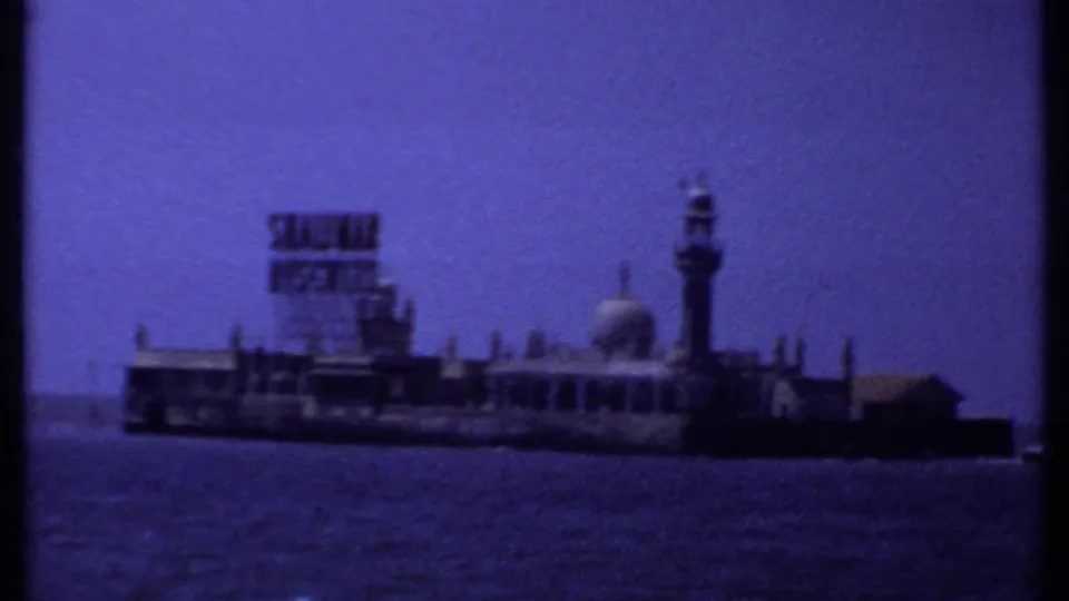 1969 India 8mm frame showing a small coastal island structure with a Satme Biscuits sign, dome, minaret, sea, and blue sky.