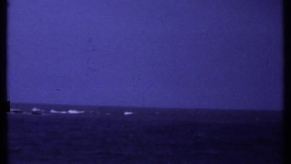 1969 India 8mm frame showing open coastal water, a distant low horizon, small white waves, and blue-purple film coloration.