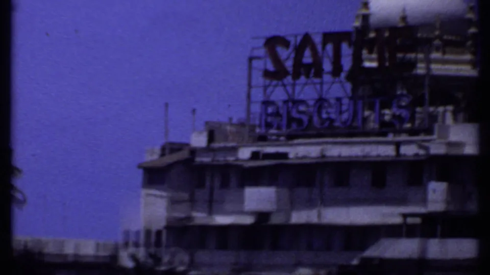 1969 India 8mm frame showing a closer view of the Satme Biscuits billboard mounted above a waterfront building.