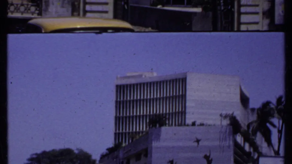 1969 India frame with a cropped exterior view of a modernist building, palms, and a hazy sky during a handheld pan.
