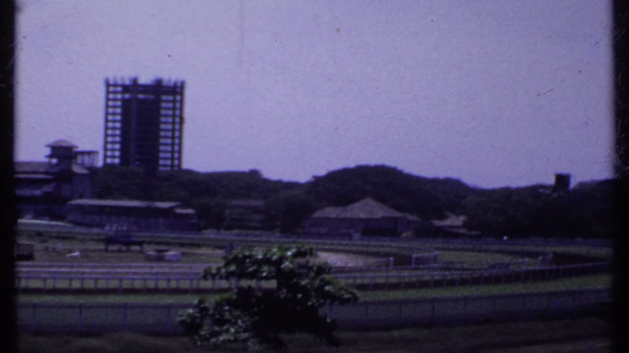Distant unfinished high-rise beyond low buildings and a track-like foreground.