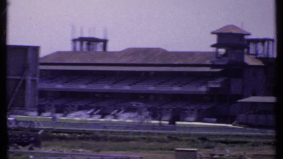 1969 India frame of a covered stadium or racetrack stand, seen from a low distant viewpoint across open grounds.