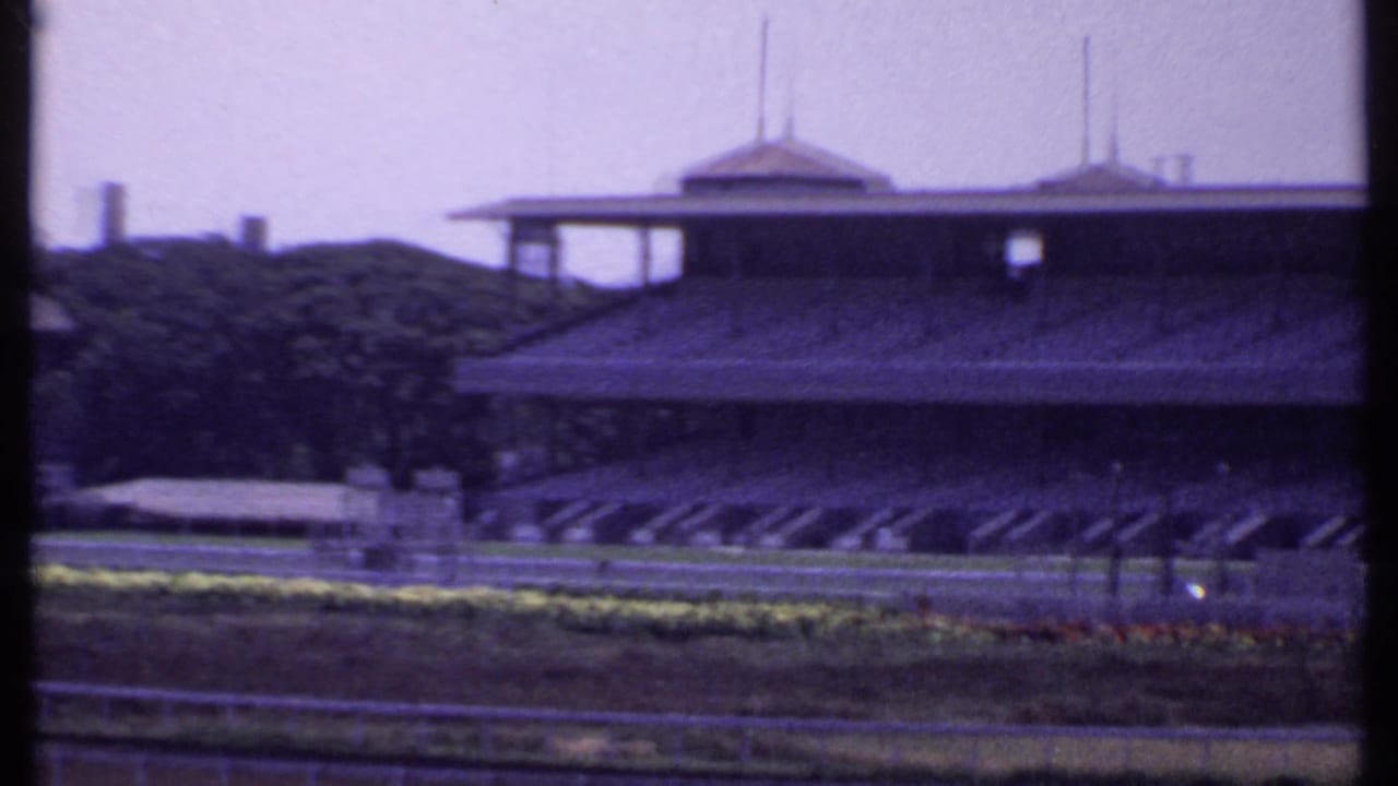 1969 India frame with an empty racetrack foreground and a large grandstand or clubhouse structure across the course.