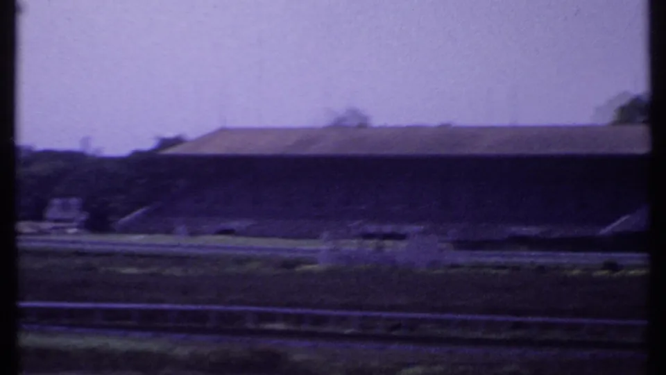 1969 India 8mm frame showing the empty racetrack and a long covered grandstand or stand building under a pale sky.