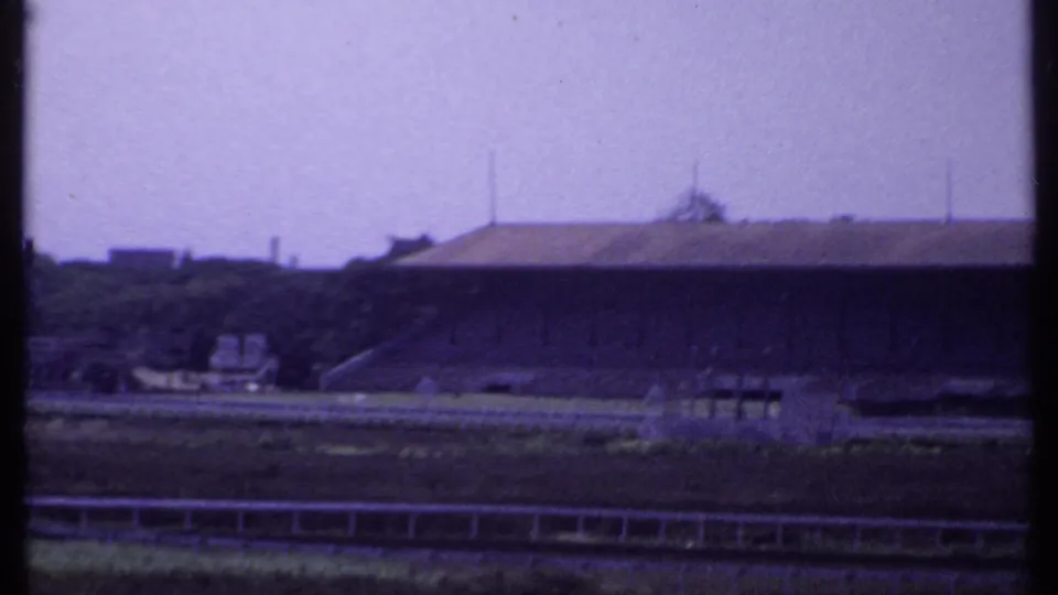 1969 India 8mm view of a distant stadium-like structure beyond open ground, with soft focus and purple color shift.