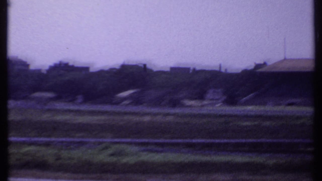 Open grounds and distant buildings with a dark vertical strip through the center.