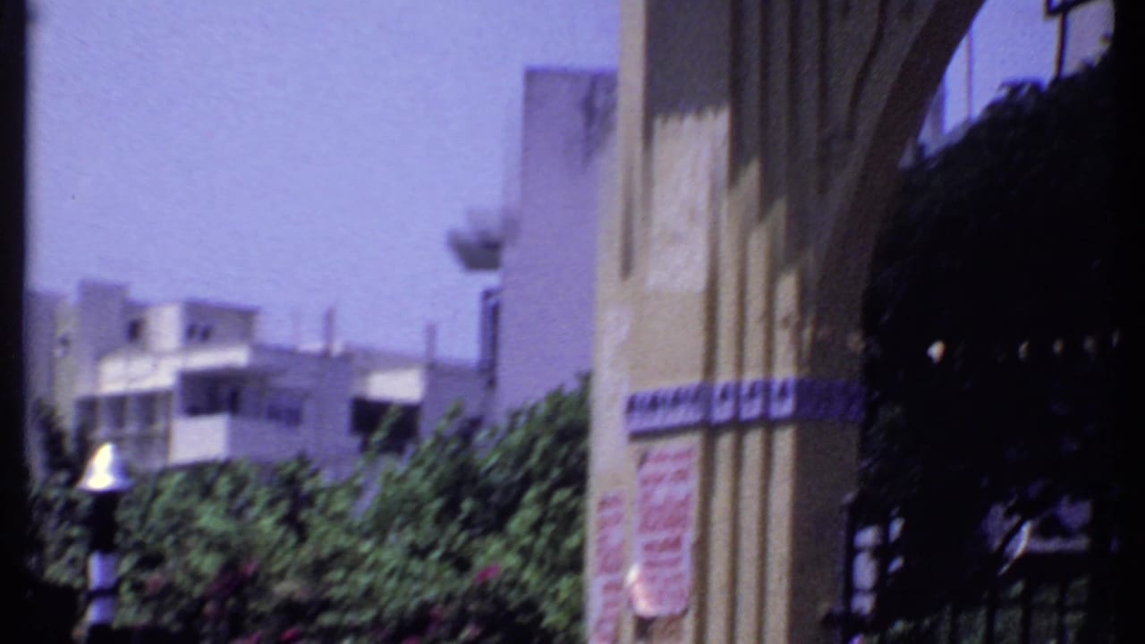 Ornate building facade with arch, awning, trees, and sunlit exterior walls.