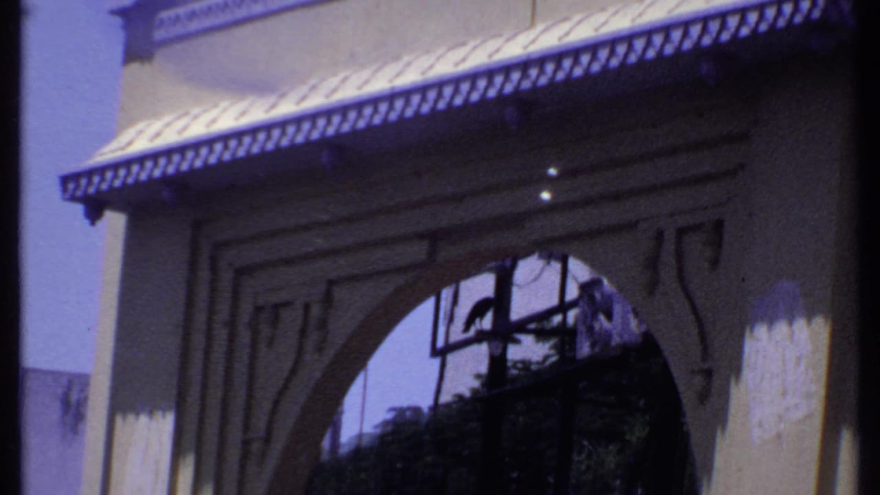 1969 India 8mm frame of a traditional-looking building entrance with a broad arch, decorative awning, and shadowed interior view.