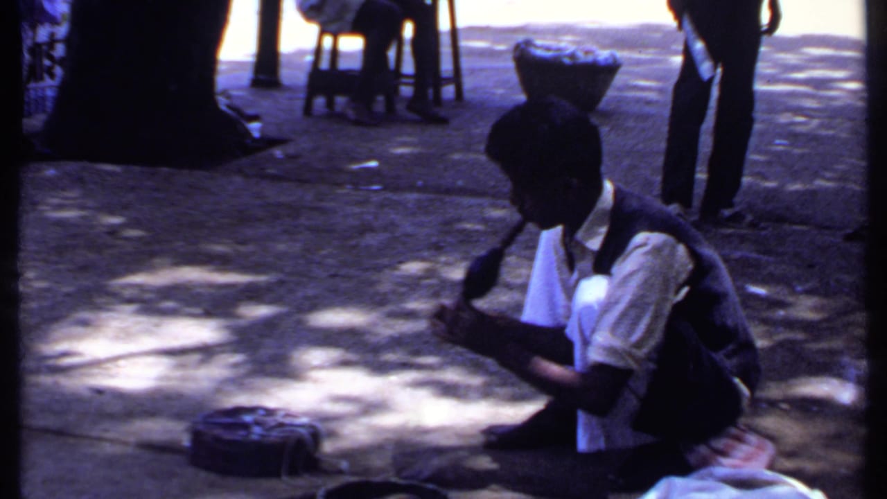 The 1969 India frame shows the crouching snake charmer and cobra from a slightly soft, dark 8mm home-movie view.