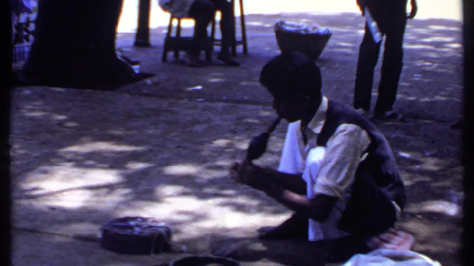 The 1969 India frame shows the crouching snake charmer and cobra from a slightly soft, dark 8mm home-movie view.