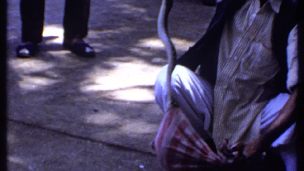 Crouching man holds a cloth bag on concrete while other legs and shoes frame the scene.