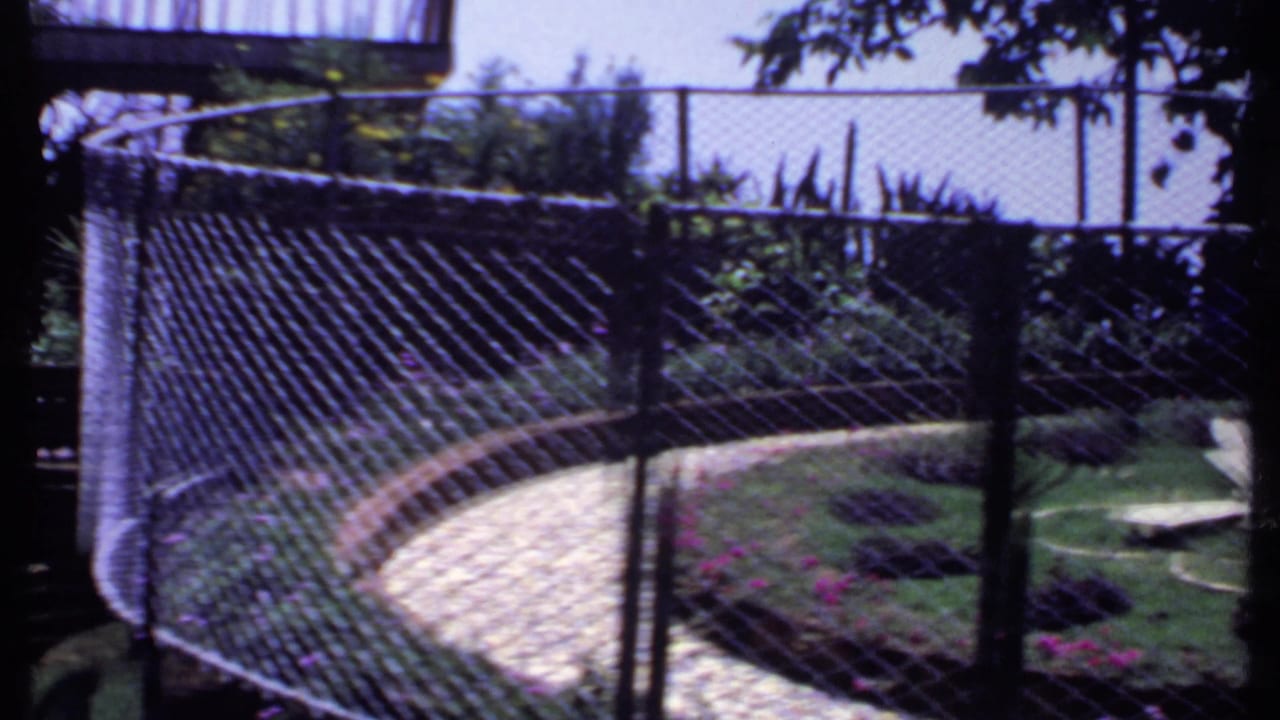 Side view of the 1969 India garden through chain-link fencing, with the curved path and airplane sculpture partly visible.