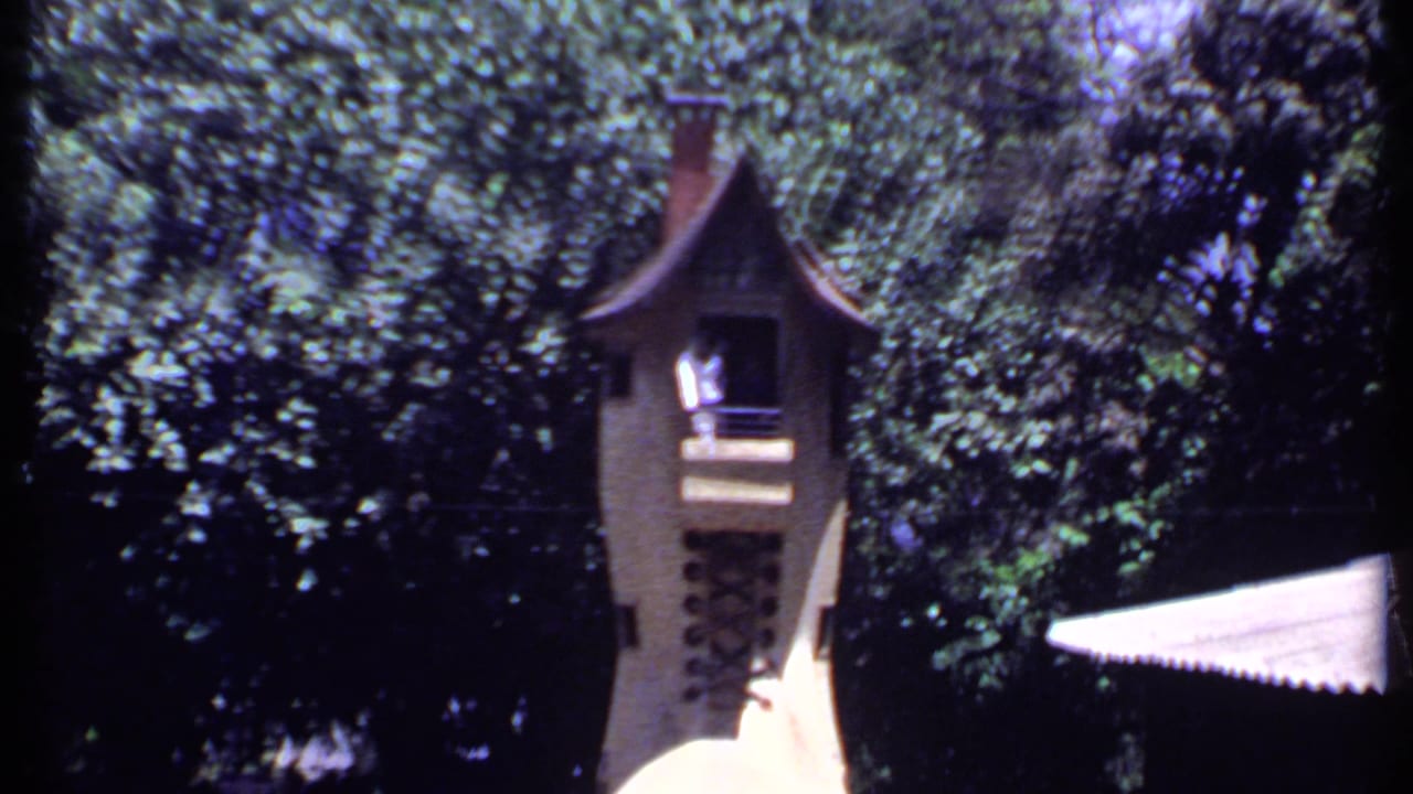 1969 India home-movie frame of an ornate tower-like park structure surrounded by dense foliage and a white awning.