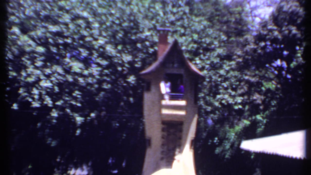 A second view of the ornate park tower in India, framed by thick greenery and a bright white awning in 8mm color footage.