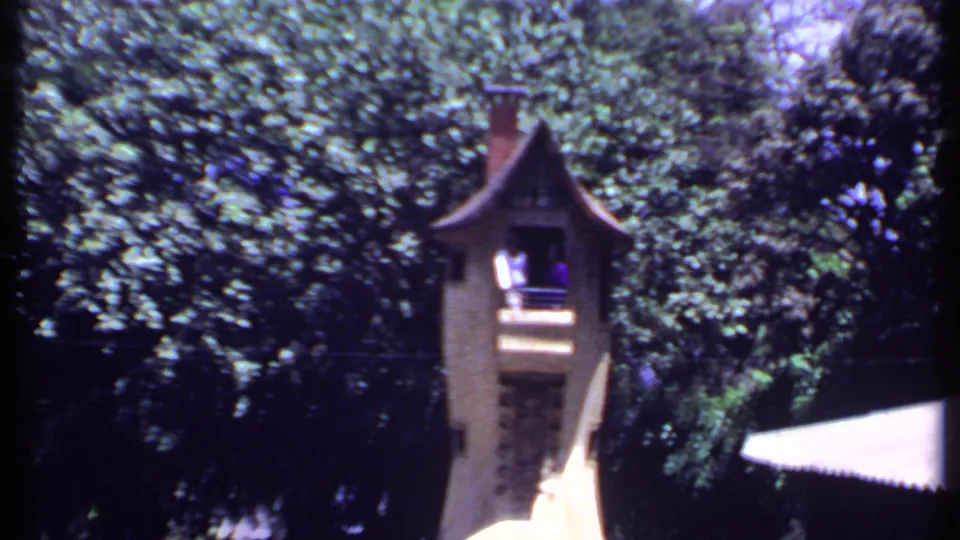 A second view of the ornate park tower in India, framed by thick greenery and a bright white awning in 8mm color footage.