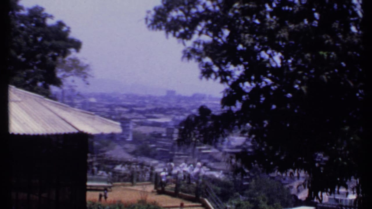 1969 India home-movie frame looking from a shaded overlook across visitors, railings, rooftops, and distant buildings in haze.