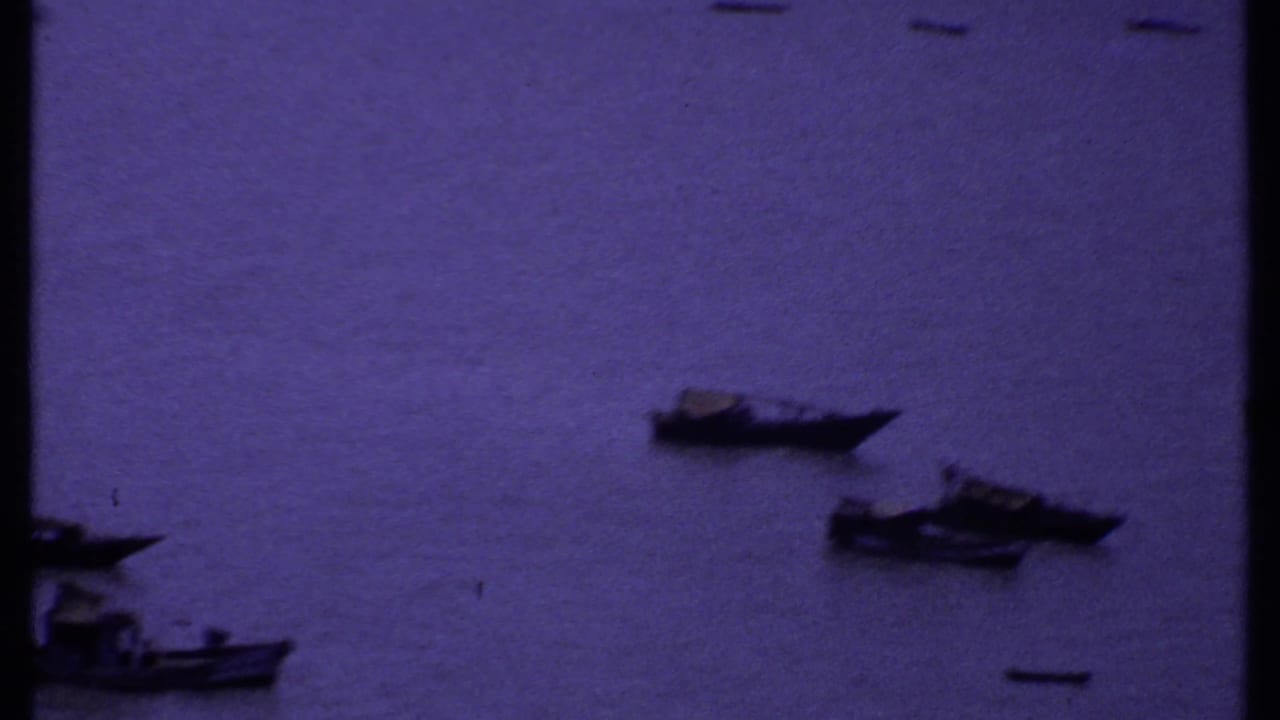 1969 India home-movie view of small boats on open coastal water, framed by dark shoreline edges.