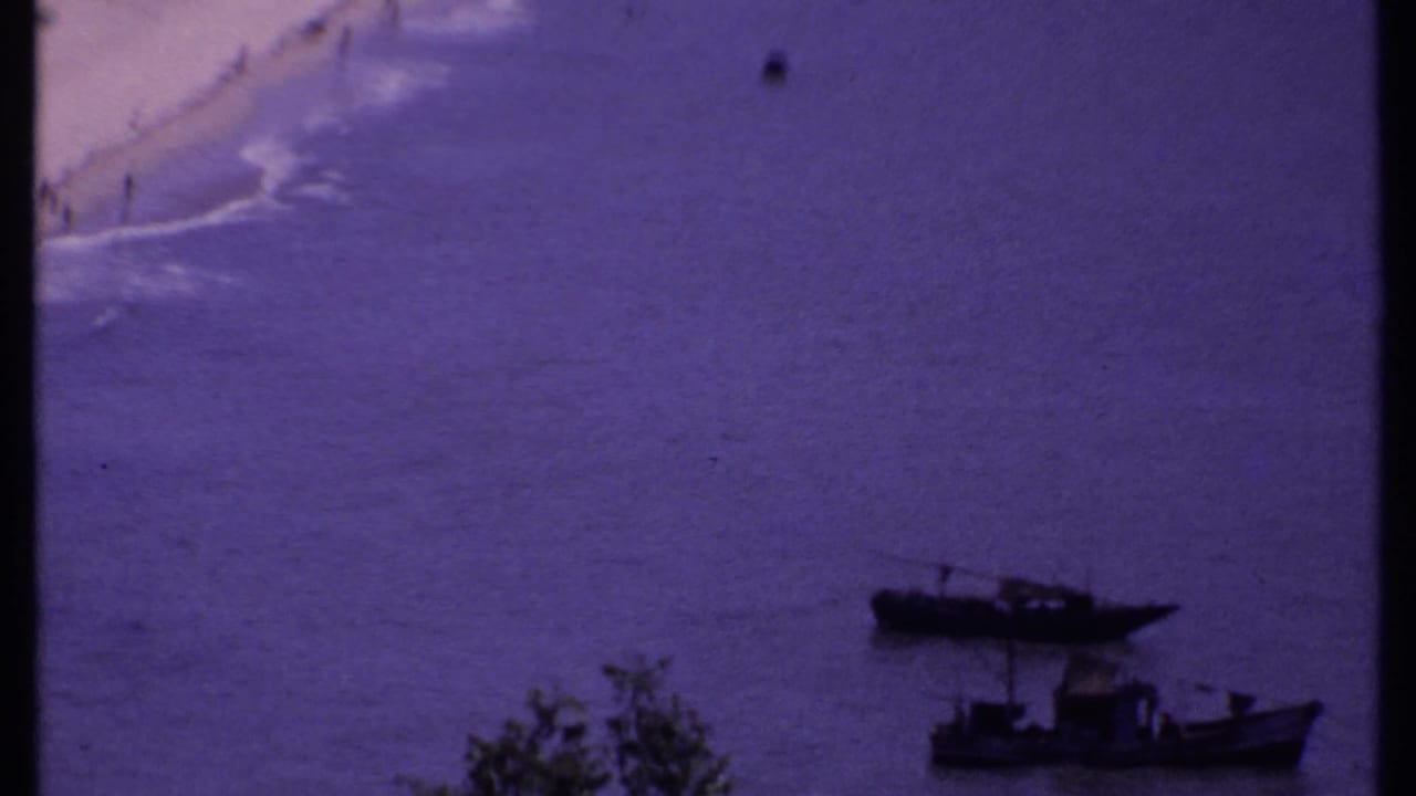 1969 India coastal frame showing a curved sandy beach, calm water, and small boats near the foreground.