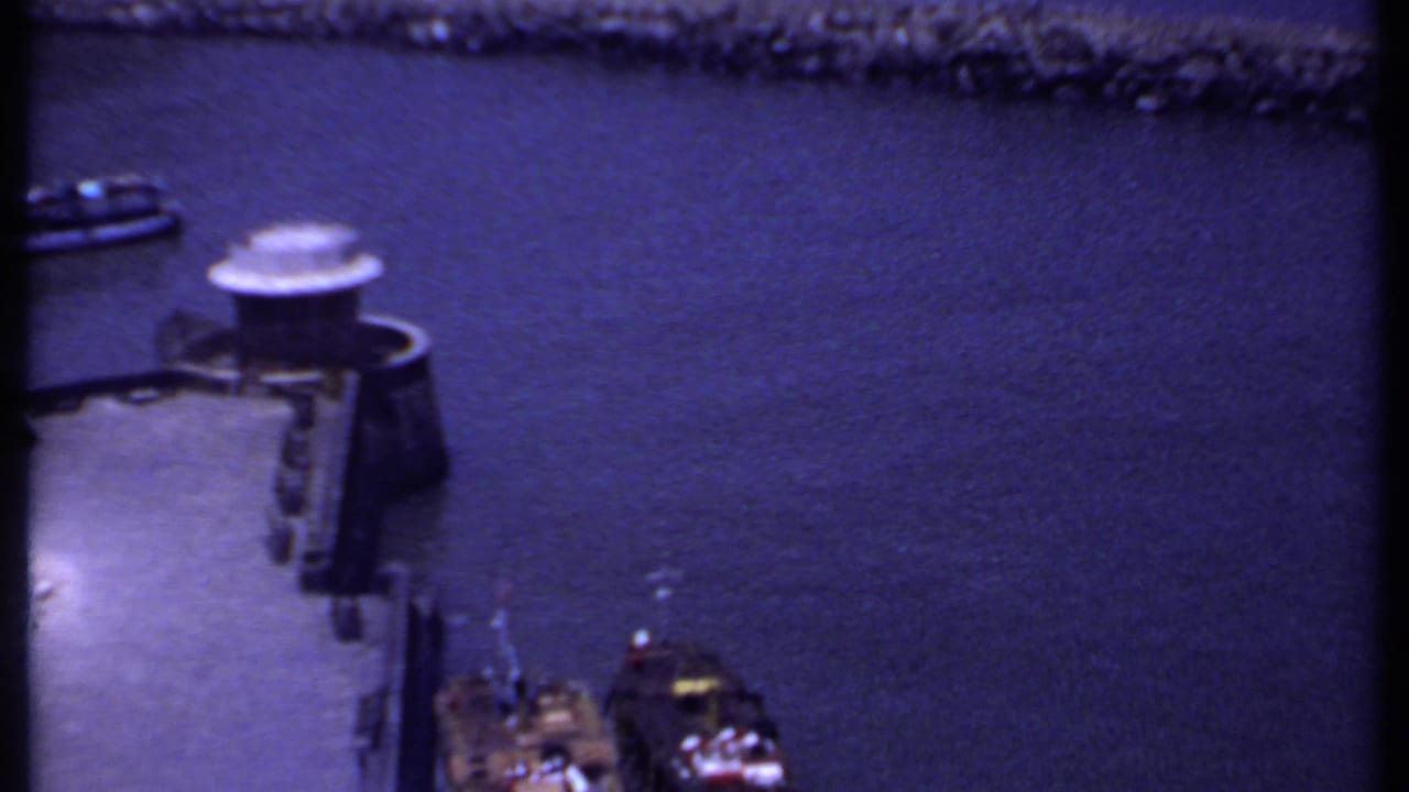 1969 India 8mm harbor view showing blue-toned water, a small boat, dock structure, and stone breakwater.